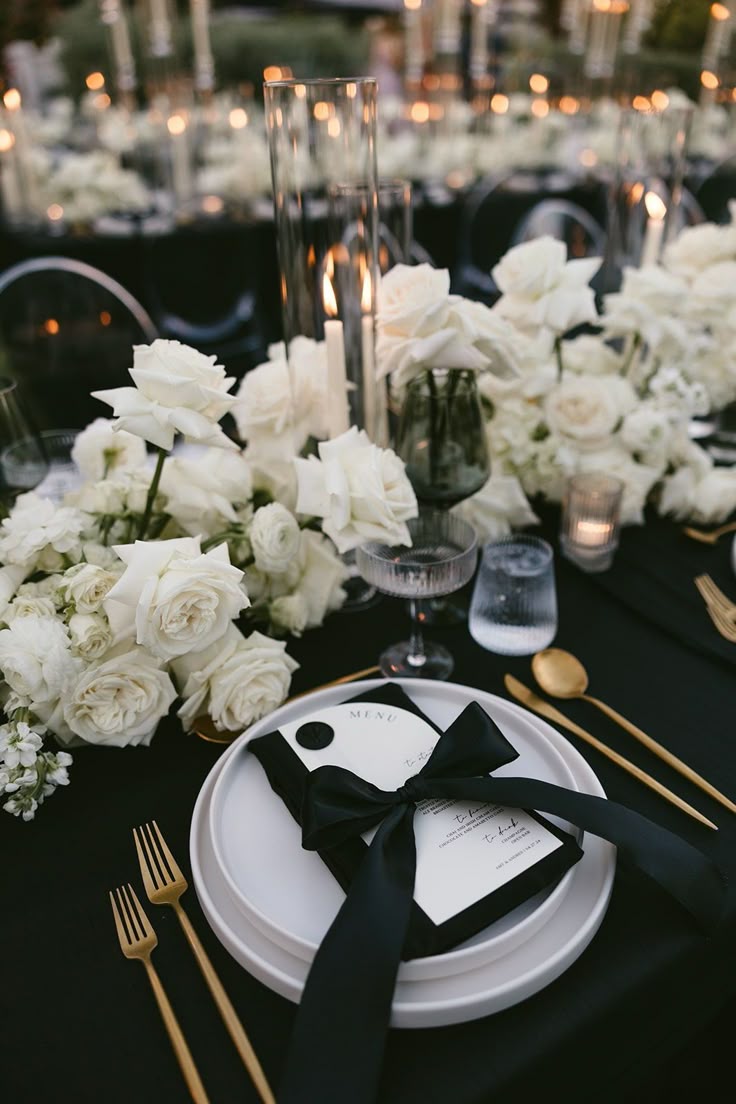 Black-tie place setting with white roses, candlelight, and gold flatware
